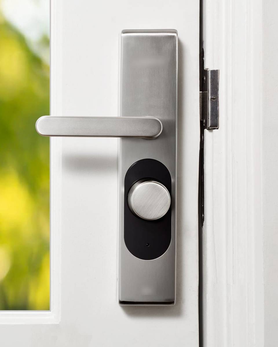 قفل ذكي فضي بمقبض على باب أبيض بجانب نافذة